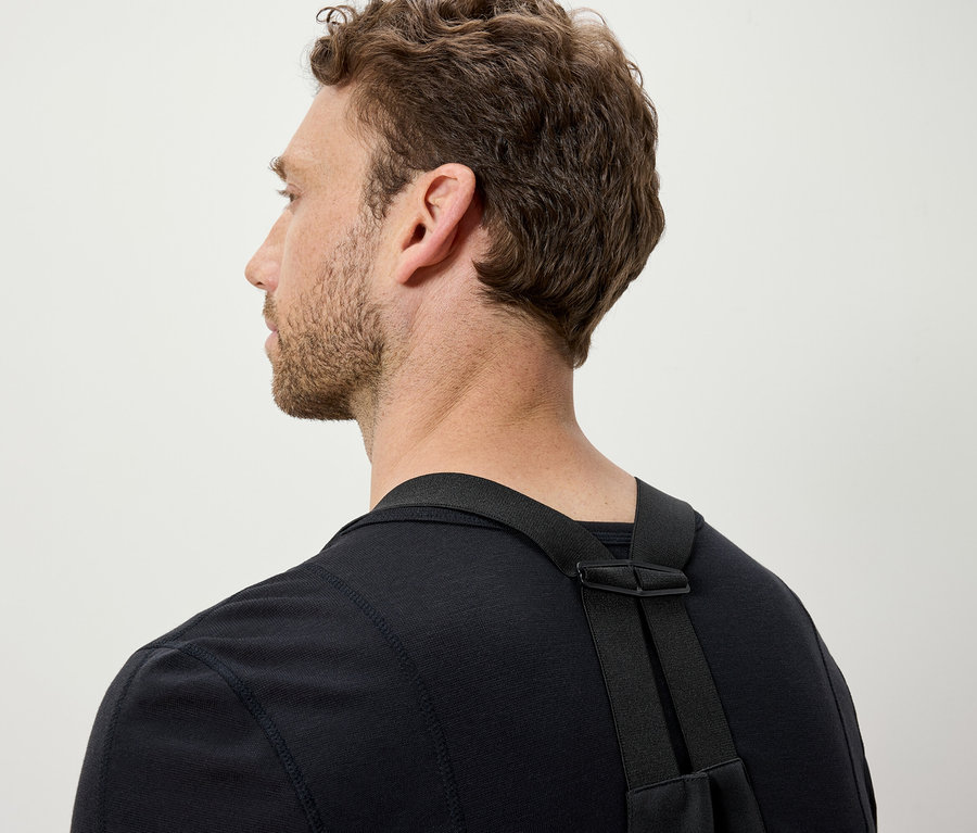 Un homme aux cheveux bruns porte un t-shirt noir et des bretelles noires.