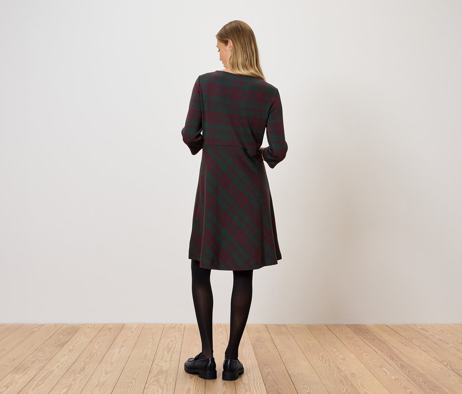 Une femme se tient dos à la caméra et porte une robe rayée, des collants noirs et des chaussures noires.