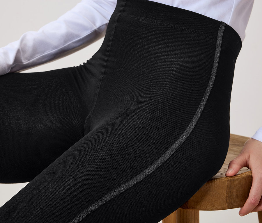 Une femme est assise sur un tabouret en bois et porte un legging noir avec une bande grise sur le côté.