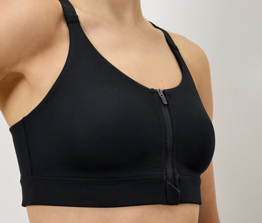 Une femme porte un soutien-gorge de sport noir avec une fermeture éclair sur le devant.