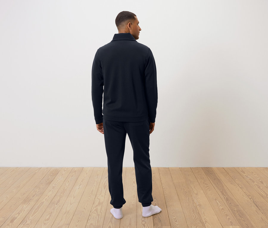 Un homme, vu de dos, porte un pyjama bleu marine et des chaussettes blanches.