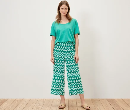 Une femme debout portant un t-shirt vert et un pantalon en satin imprimé.