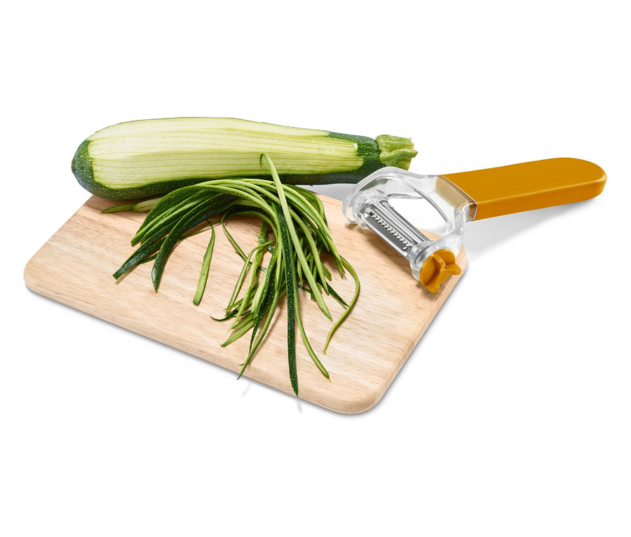 Moitié de courgette, lamelles de courgette et une râpe à manche orange sur une planche en bois.