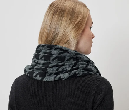 Une femme porte un foulard pied-de-poule gris et noir et un pull noir.