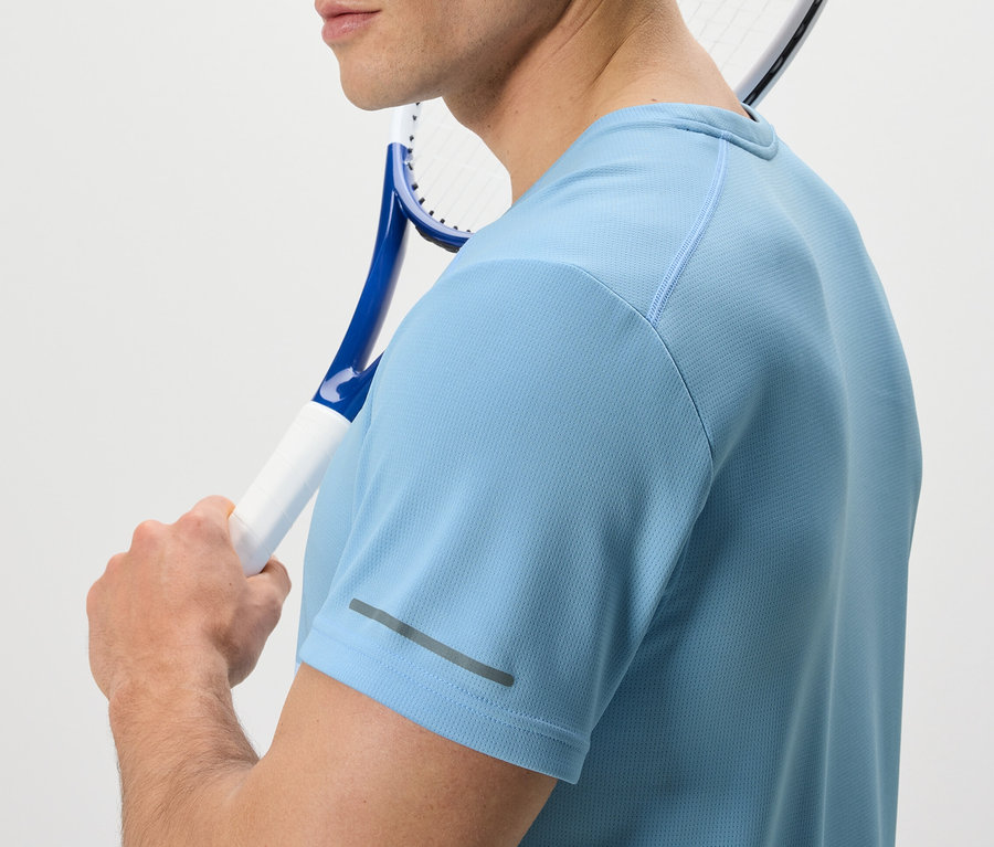 Un homme portant un t-shirt fonctionnel bleu clair tient une raquette de tennis sur son épaule.