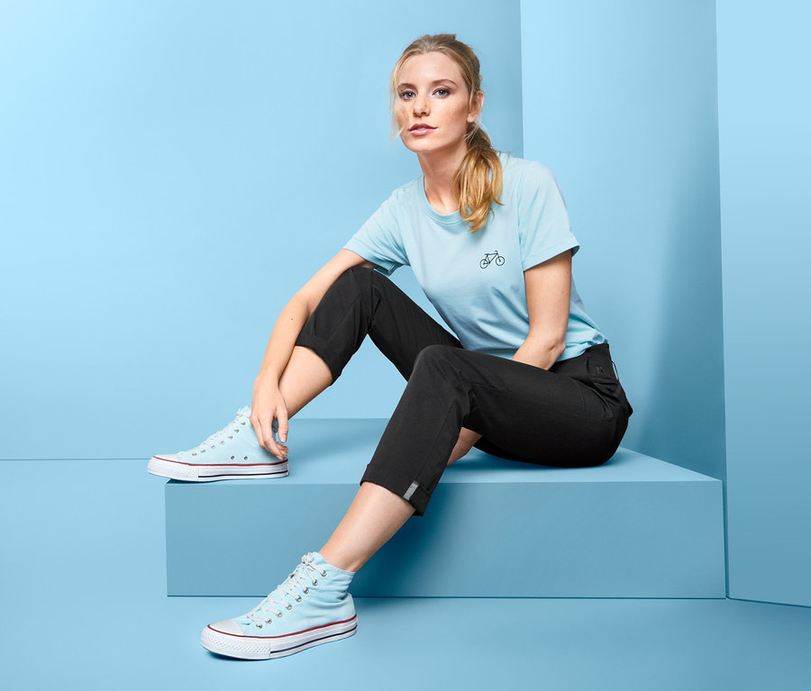 Une femme est assise sur un fond bleu et porte un pantalon fonctionnel.