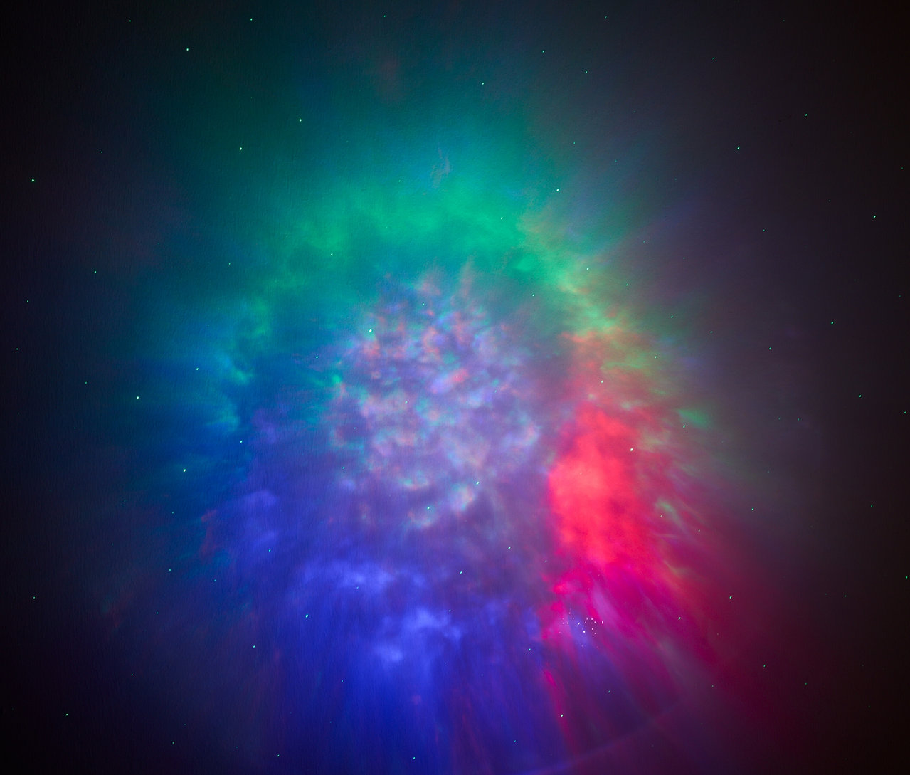 Une nébuleuse avec des nuances de vert, de rouge et de bleu sur un fond sombre.