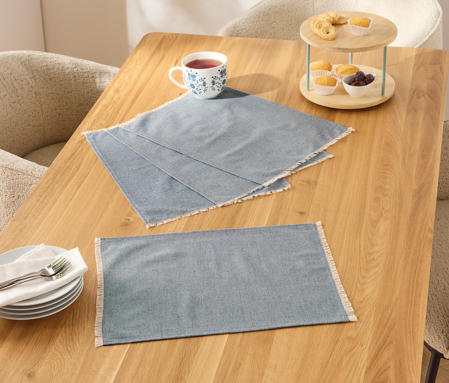 Deux sets de table bleus à bordure blanche sur une table en bois, à côté d'une tasse, d'assiettes et d'un présentoir à gâteaux avec de la nourriture.