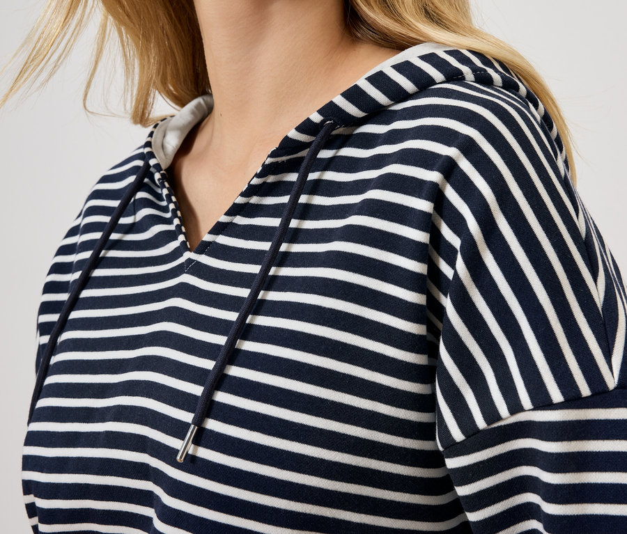 Une femme blonde porte un sweat à capuche rayé bleu et blanc.