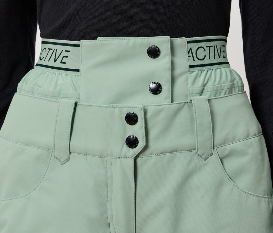 Détail d'un pantalon vert clair avec des boutons noirs et l'inscription "ACTIVE" sur la ceinture.