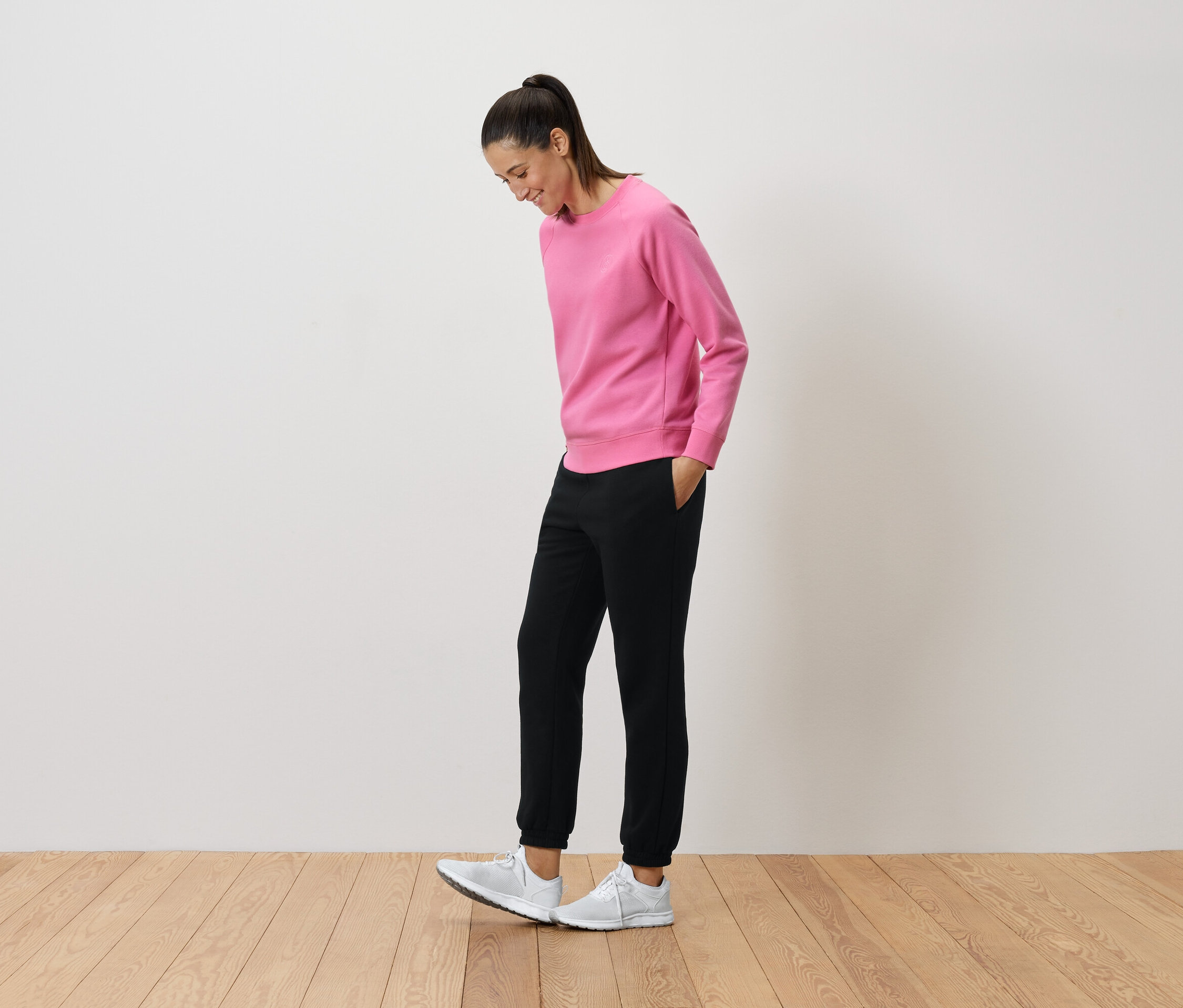 Femme en pull rose et pantalon noir regardant ses baskets blanches.