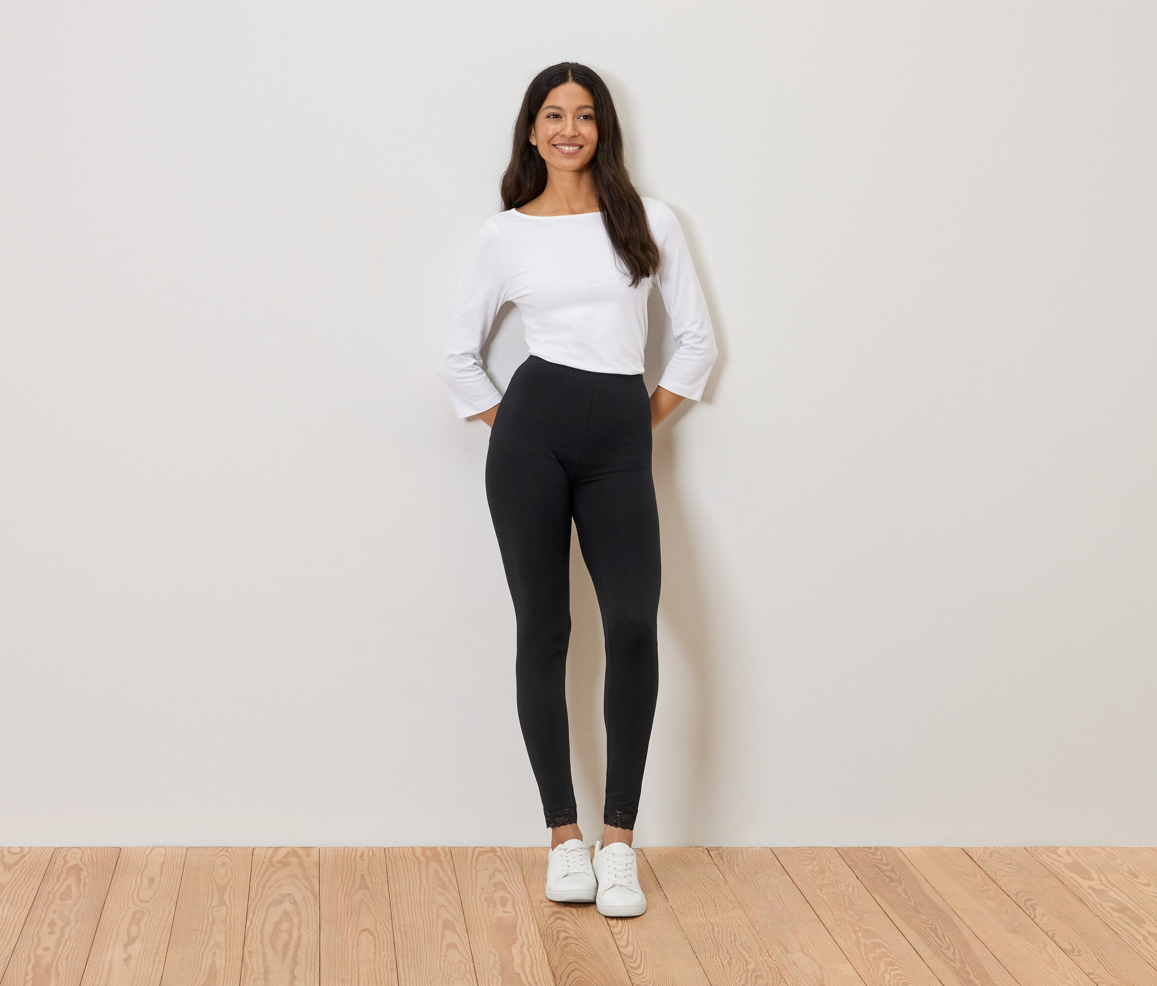 Femme debout devant un mur portant un haut blanc, un legging noir et des baskets blanches.