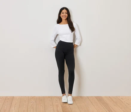 Femme debout devant un mur portant un haut blanc, un legging noir et des baskets blanches.