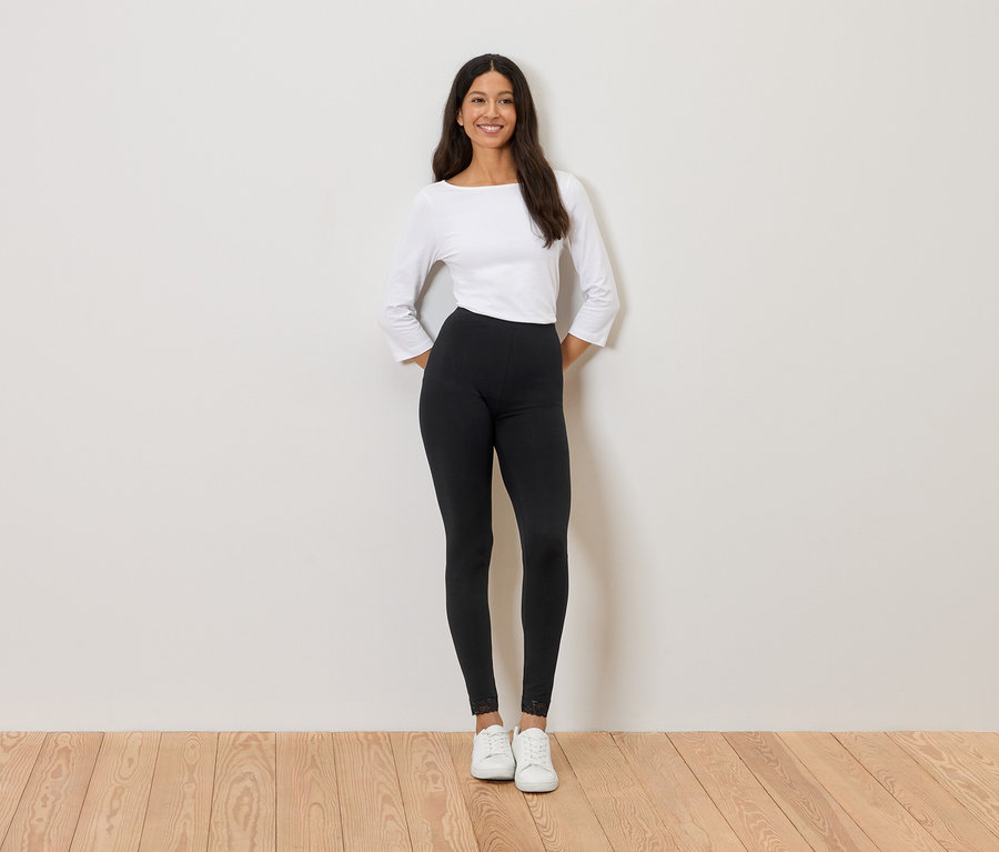 Femme debout devant un mur portant un haut blanc, un legging noir et des baskets blanches.