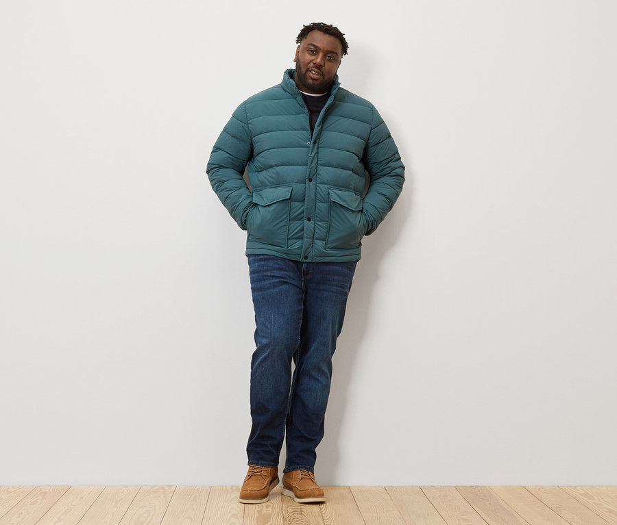 Un homme debout portant une veste matelassée, un jean et des chaussures.