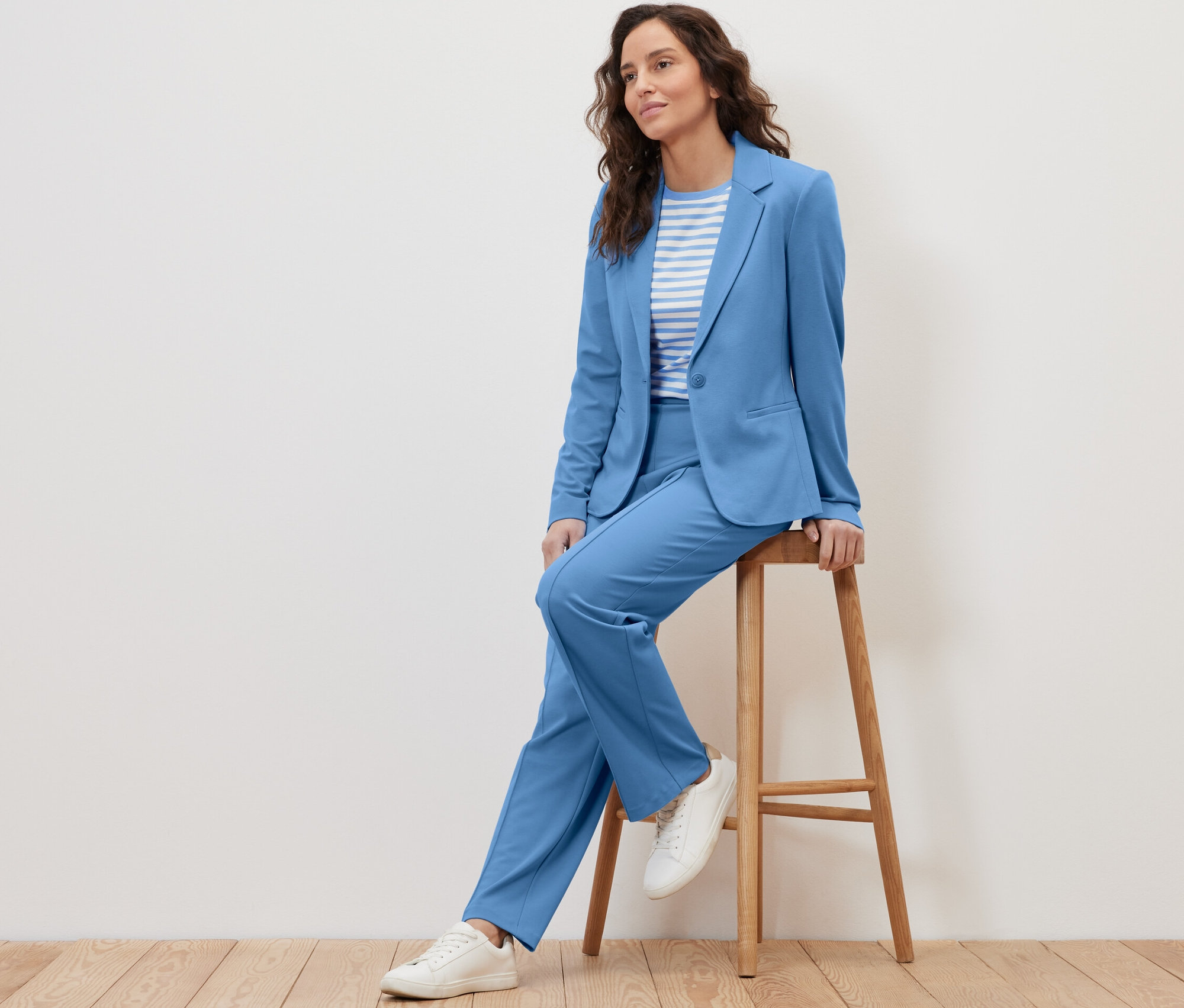 Une femme est assise sur un tabouret et porte un blazer en jersey bleu clair.