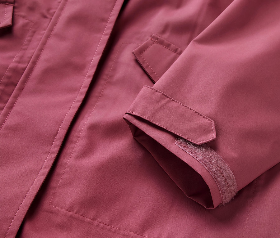 Gros plan sur une parka de pluie pour enfant, veste rose avec poches et poignets ajustables.