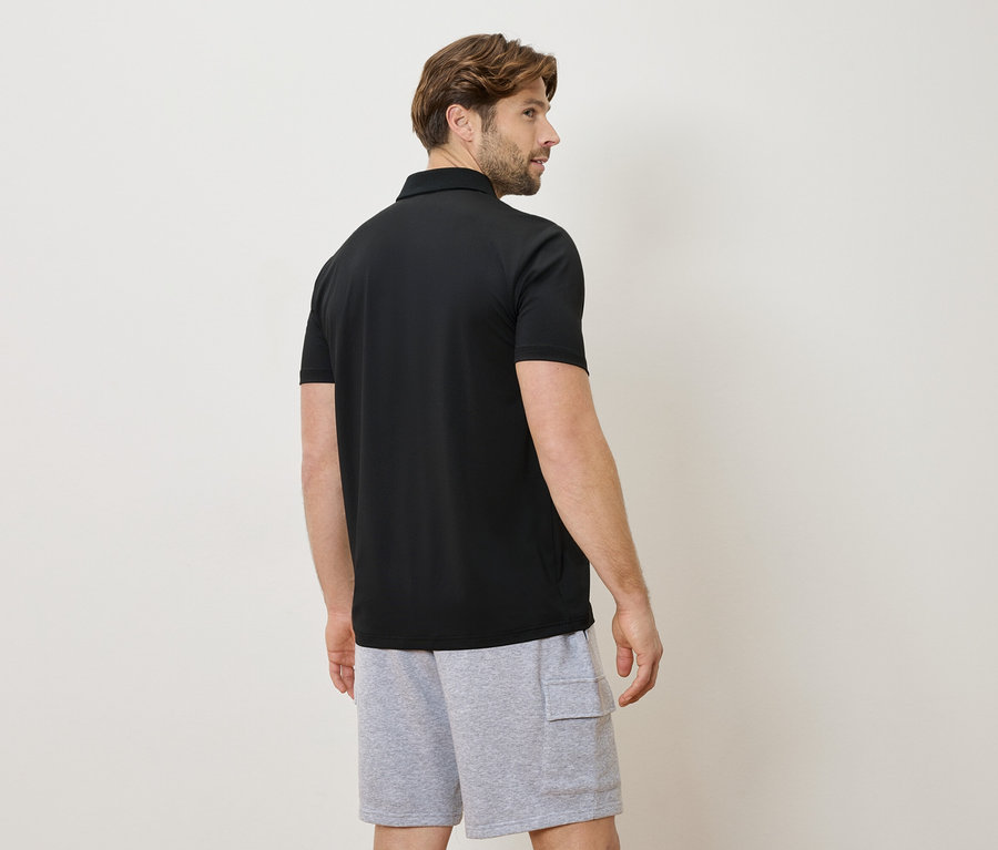 Homme vu de dos portant un polo noir et un short gris.