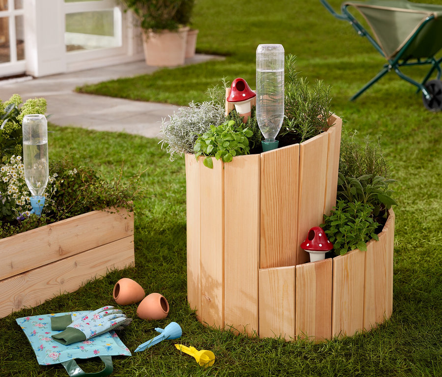 Sur une pelouse se trouve un potager surélevé en bois « Escargot », planté d'herbes aromatiques et de légumes.