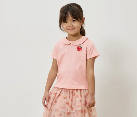 Fillette portant un t-shirt rose avec une application de fraise et une jupe rose avec un motif de fraises.