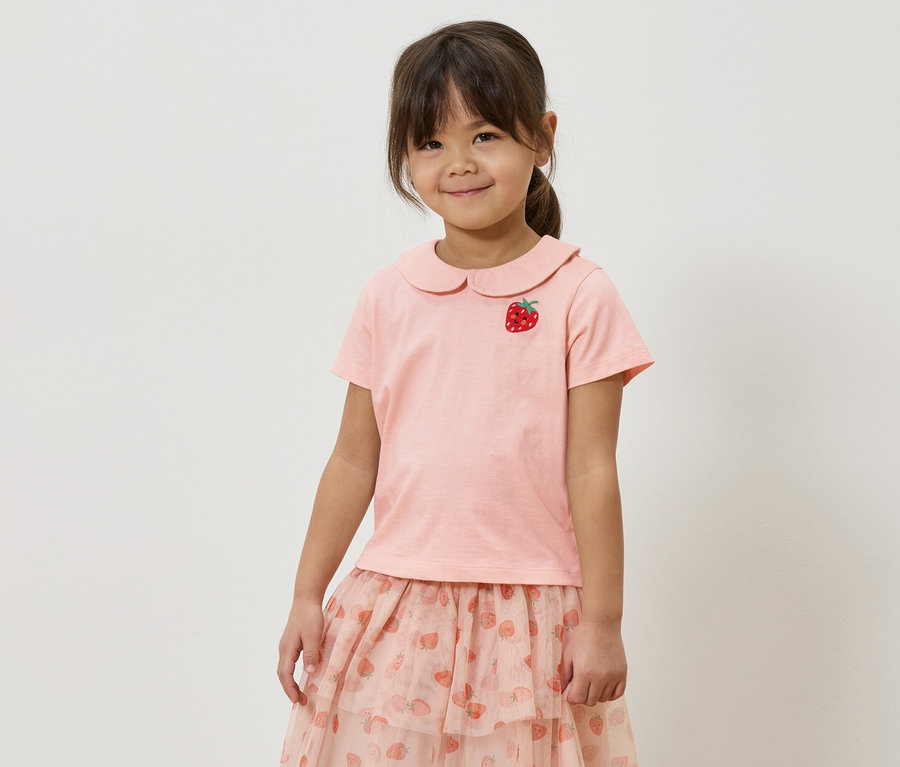 Fillette portant un t-shirt rose avec une application de fraise et une jupe rose avec un motif de fraises.