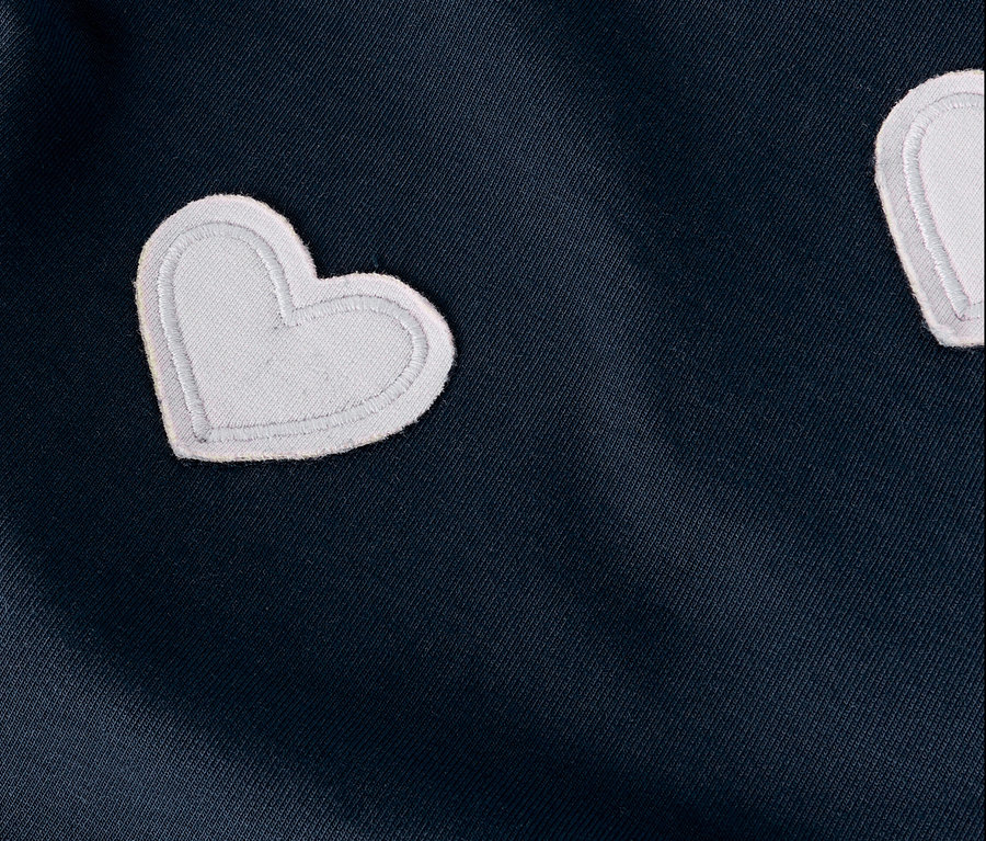 Gros plan d'un tissu bleu marine avec des applications en forme de cœur blanches.