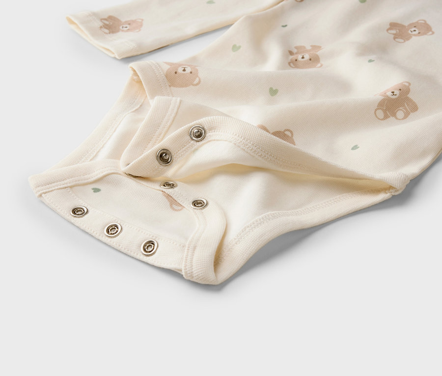 Gros plan d'un body clair pour bébé avec motif oursons et cœurs, et boutons-pression à l'entrejambe.