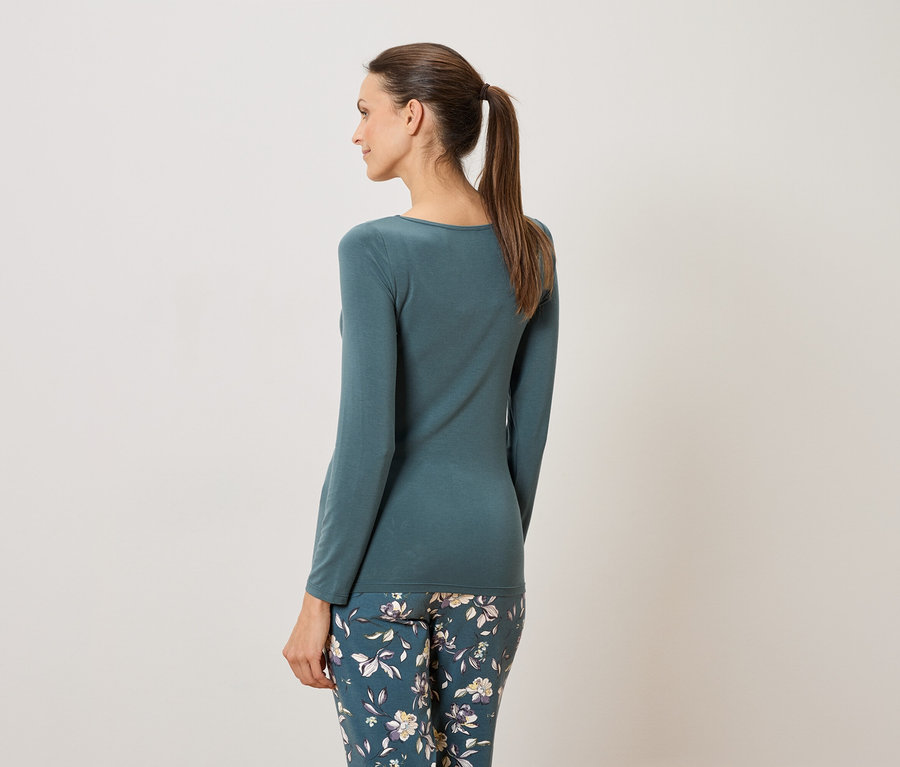 Femme vue de dos portant un haut bleu-vert à manches longues et un pantalon à fleurs.