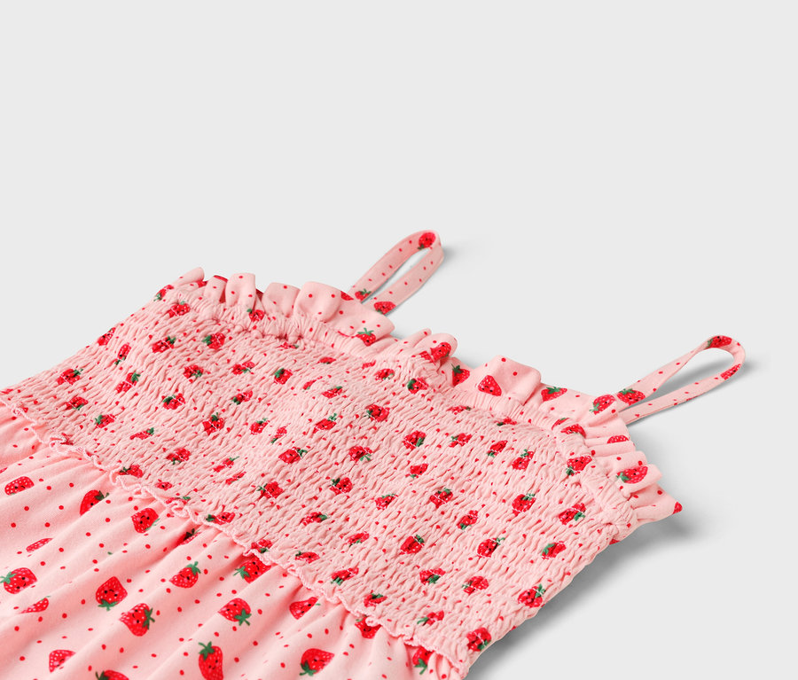 Gros plan d'une robe rose à motifs de fraises, avec un buste smocké et des volants.