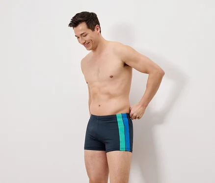 Un homme porte un maillot de bain bleu marine avec des rayures vertes et bleues.
