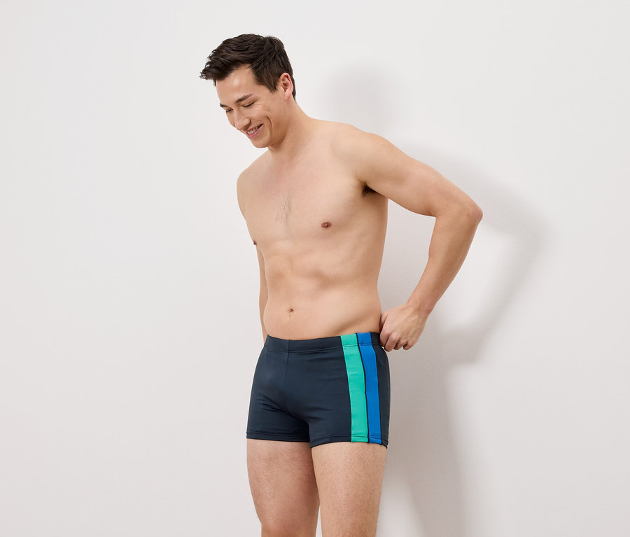 Un homme porte un maillot de bain bleu marine avec des rayures vertes et bleues.