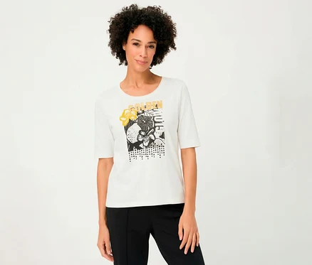 Une femme porte un T-shirt 3/4 Olsen blanc avec un motif floral et un pantalon noir.
