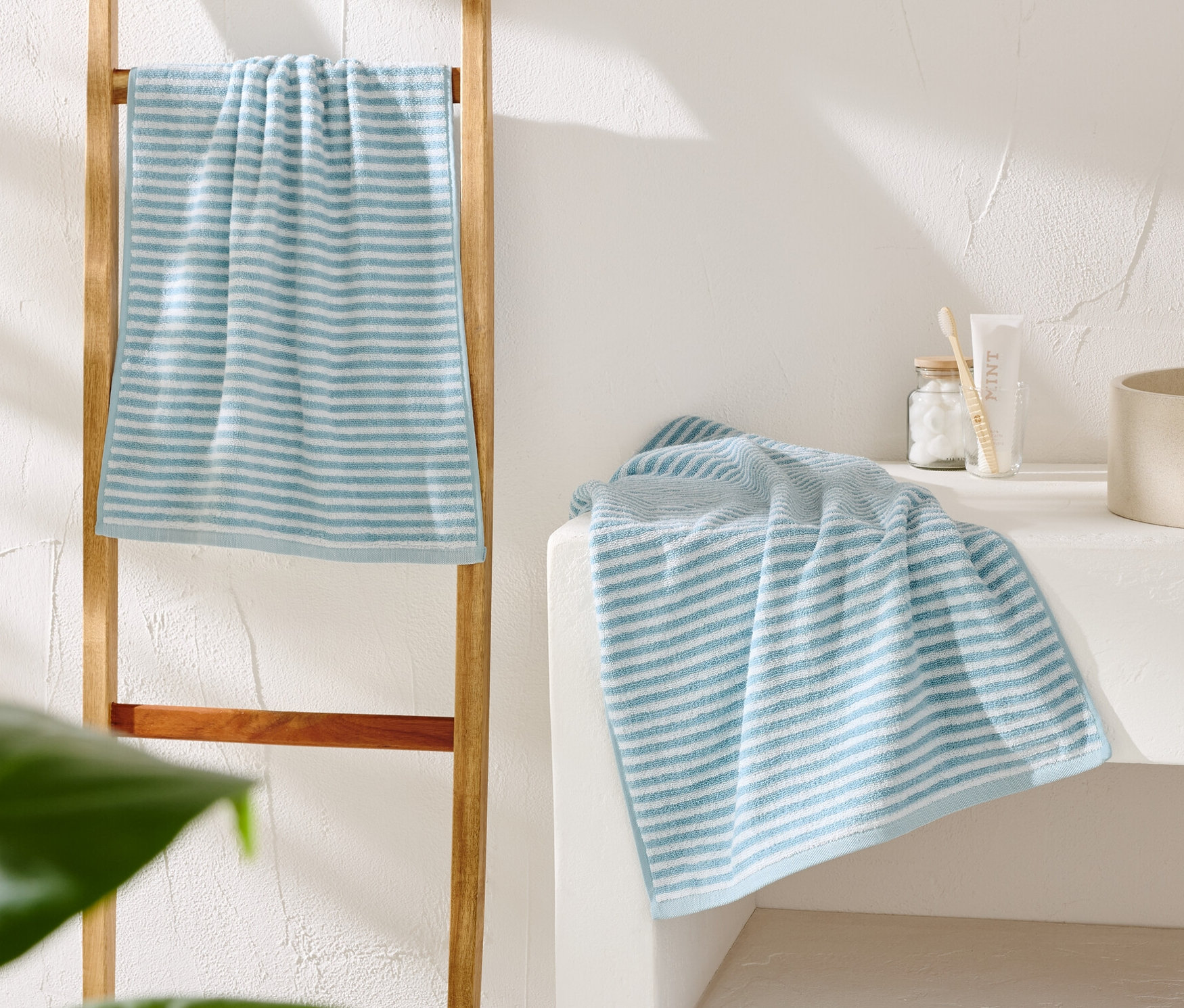 Une serviette rayée bleu et blanc est suspendue à une échelle en bois. Une autre serviette est posée à côté d'un lavabo beige.