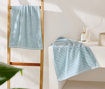 Une serviette rayée bleu et blanc est suspendue à une échelle en bois. Une autre serviette est posée à côté d'un lavabo beige.