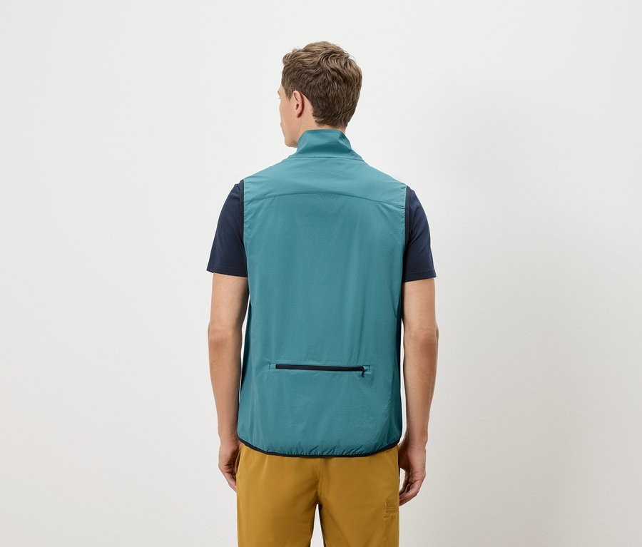 Homme vu de dos portant un t-shirt bleu marine et un short doré, portant un gilet pétrole avec une poche zippée.