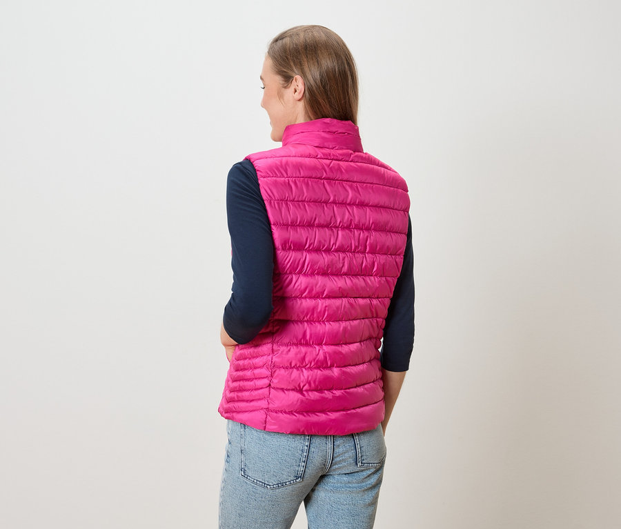 Femme vue de dos portant une veste matelassée rose sur un t-shirt à manches longues bleu marine et un jean.