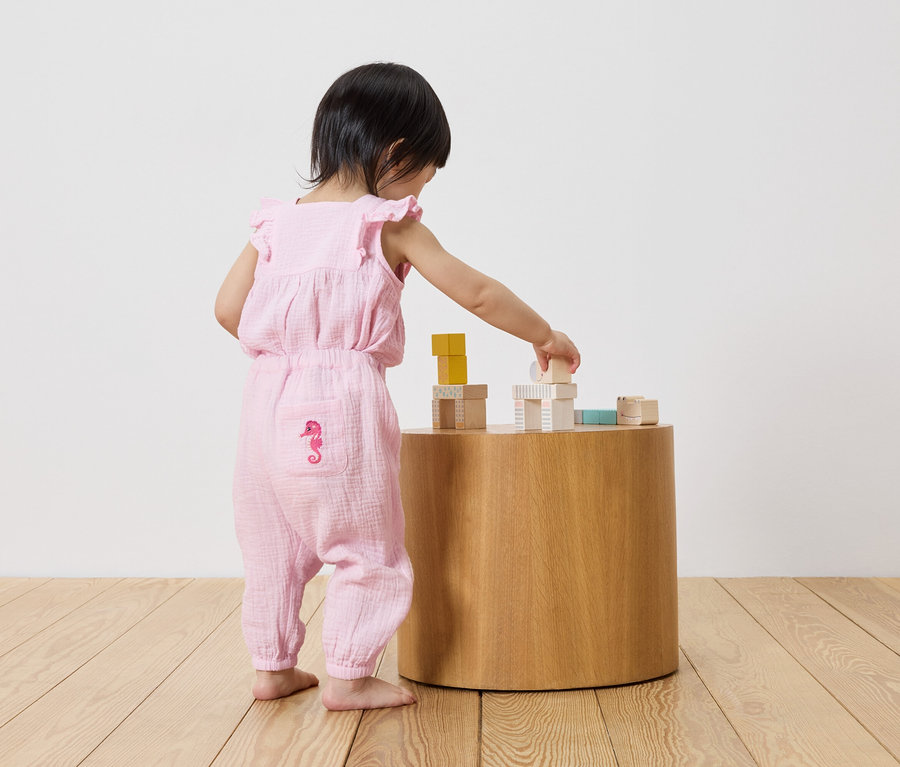 Un jeune enfant en combinaison rose à motif d'hippocampe joue avec des blocs de construction sur une table ronde en bois.
