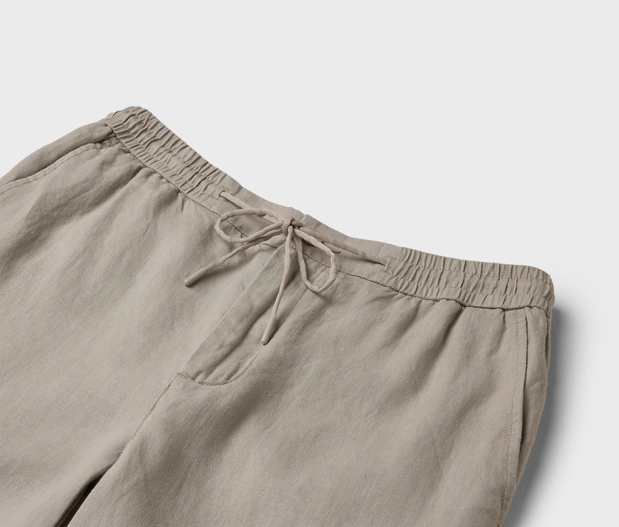Gros plan sur un pantalon en lin beige avec cordon de serrage et taille élastique.