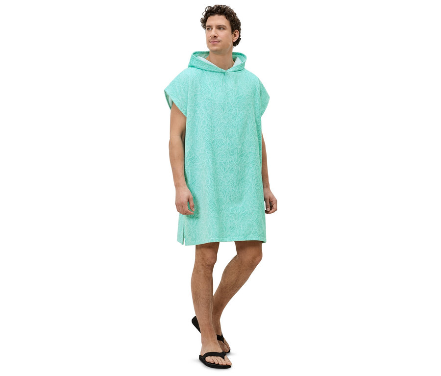 Un homme se tient de profil, portant un poncho à capuche turquoise à motifs et des sandales noires.