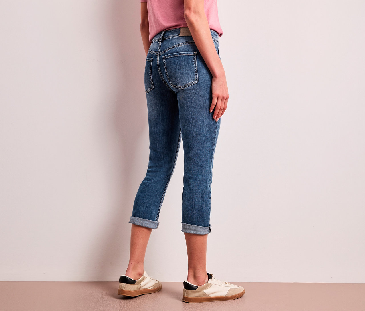 Une personne de dos, portant un jean 7/8 Street One « Jane » bleu retroussé et des baskets claires.