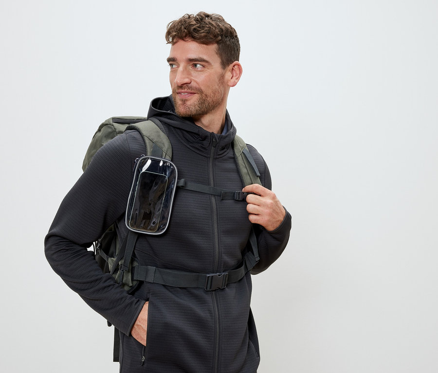 Homme portant un sac à dos vert olive avec un étui de téléphone transparent sur les bretelles.