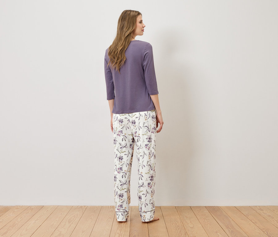 Femme debout dos à la caméra portant un haut de pyjama violet et un pantalon de pyjama blanc à motifs floraux.