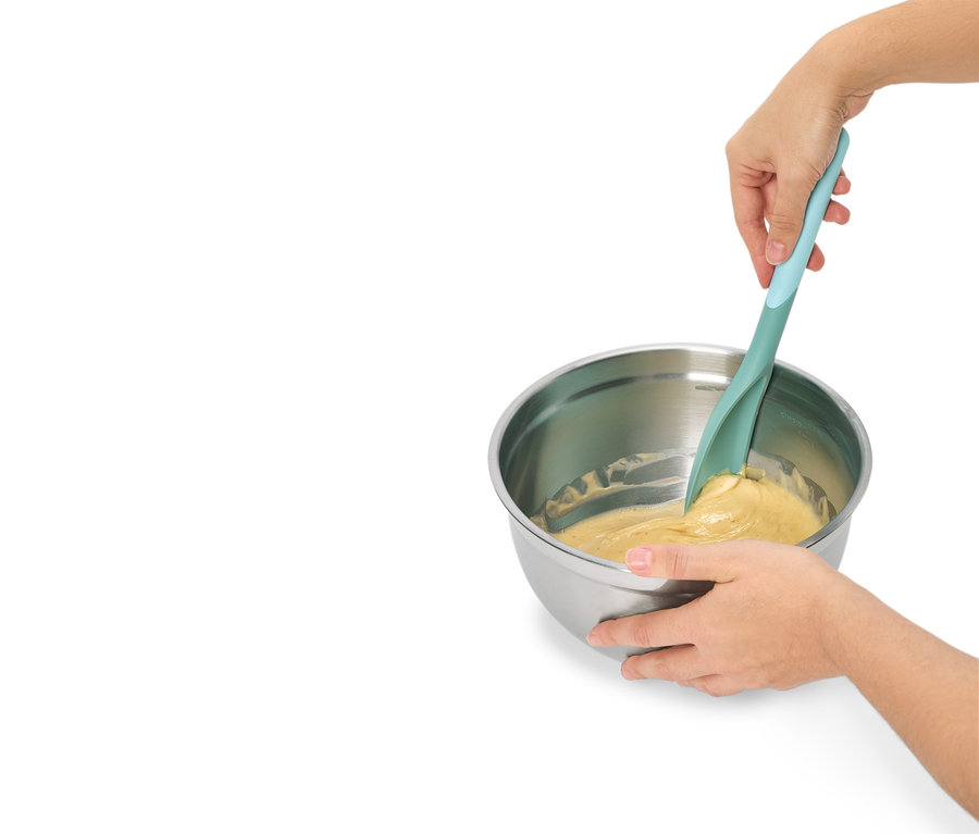 Des mains mélangent de la pâte dans un bol en acier inoxydable avec une spatule turquoise.