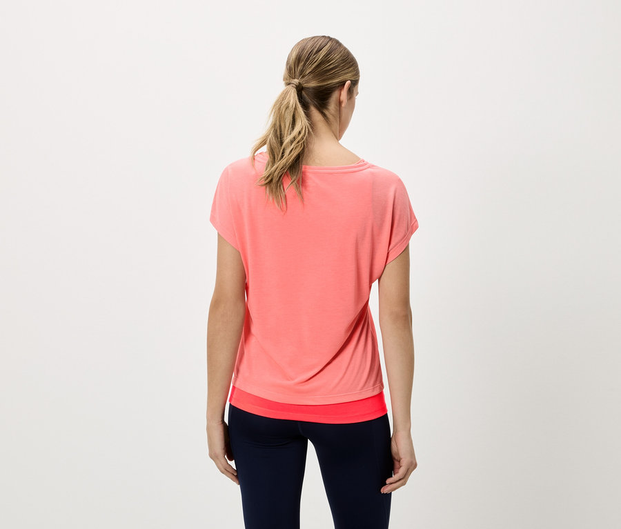 Vue de dos d'une femme blonde portant un t-shirt corail et un legging bleu marine.