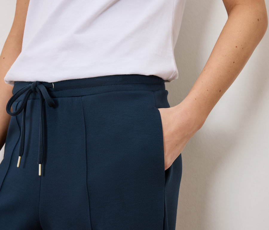 Gros plan d'une femme portant un pantalon de survêtement bleu marine avec cordon de serrage et détails dorés et un t-shirt blanc.