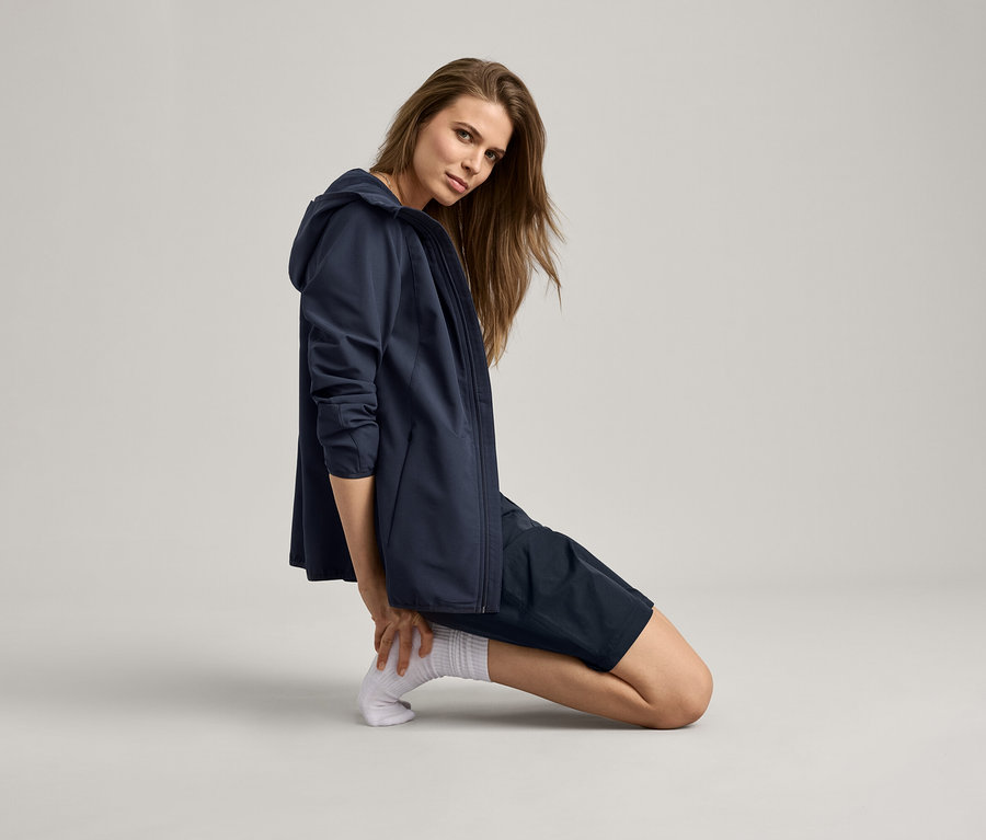 Femme agenouillée portant une veste bleu marine et un short.