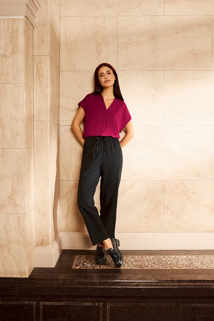 Femme posant en pantalon en lin noir et mocassins en cuir contre un mur.