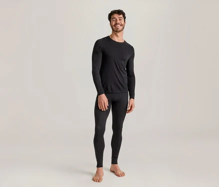 Homme souriant portant un haut thermique noir à manches longues et un legging thermique noir, debout pieds nus.