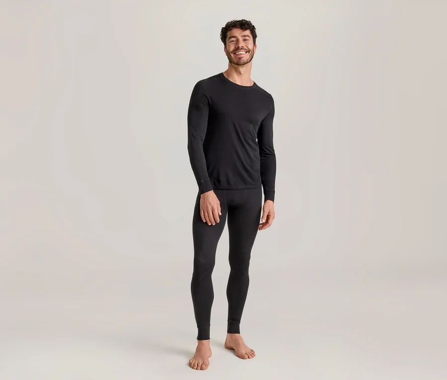 Homme souriant portant un haut thermique noir à manches longues et un legging thermique noir, debout pieds nus.