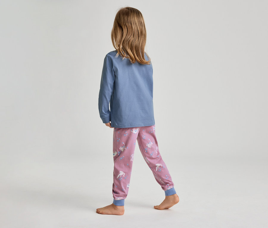Un enfant, vu de dos, avec de longs cheveux bruns, porte un haut bleu à manches longues et un pantalon de pyjama rose à motifs de licornes et d'étoiles. L'enfant est pieds nus sur un sol gris clair.